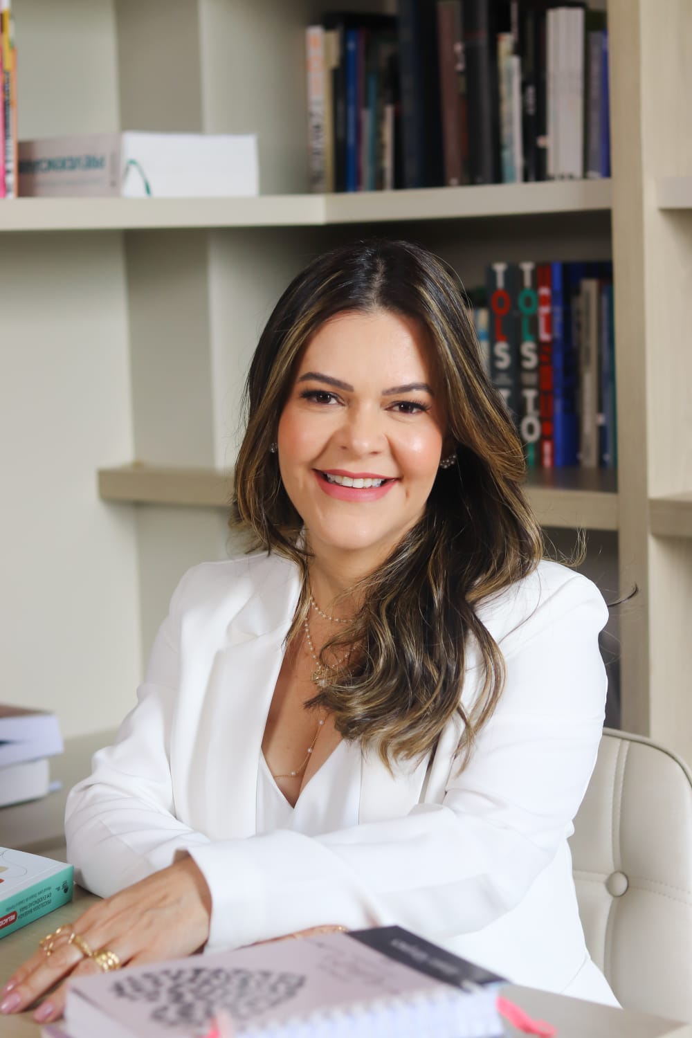 Almira Marques sentada em seu consultório, ao lado da estante de livros